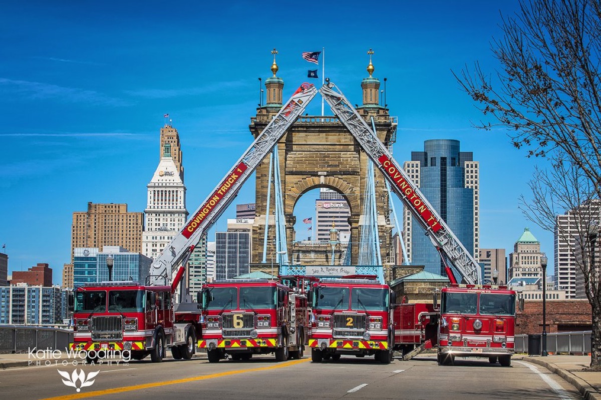 Covington fire trucks lined up under the Roebling Bridge with the Cincinnati skyline